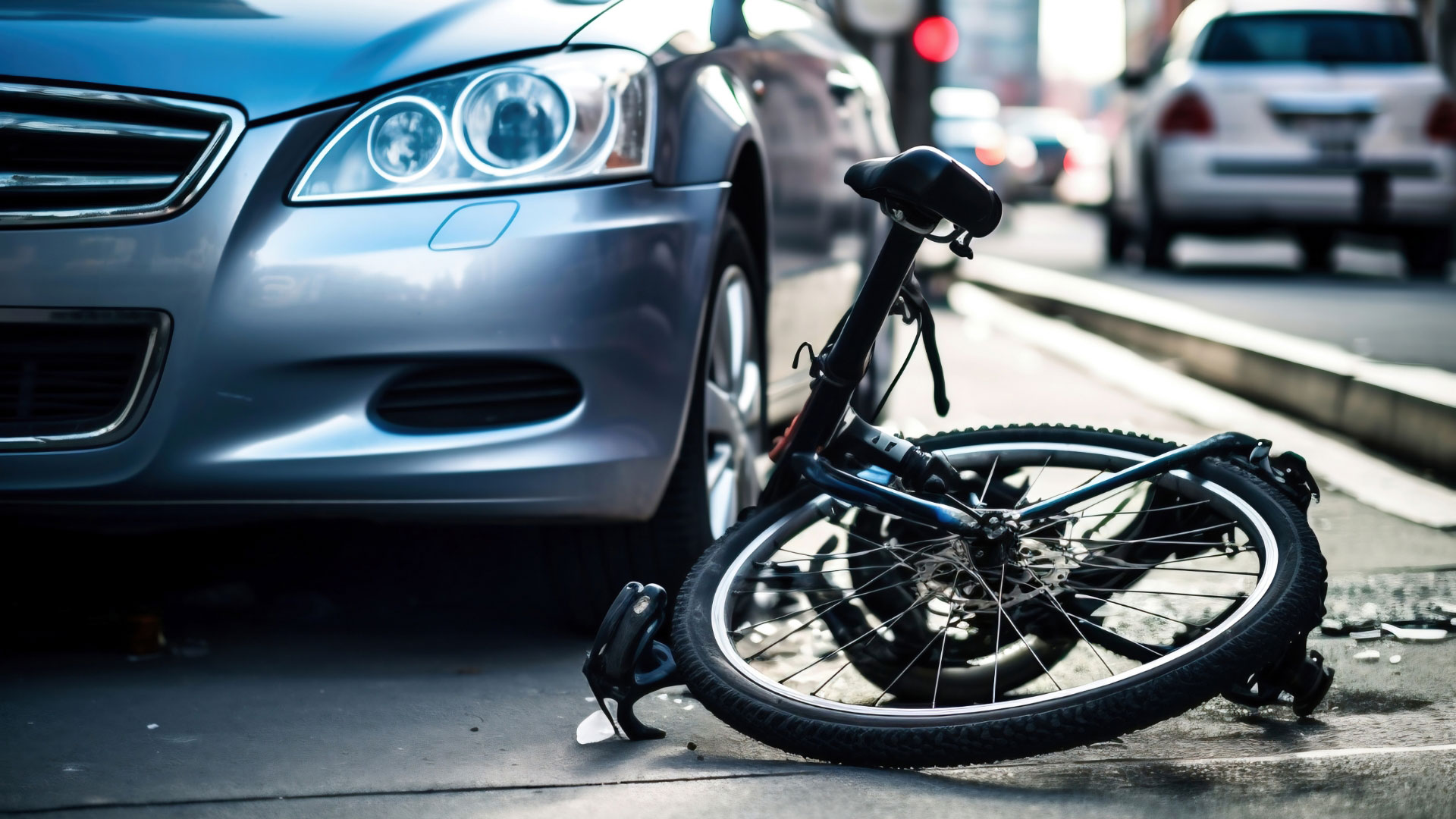 Bicycle lying on its side after a collision with a parked car on a city street, with traffic blurred in the background.